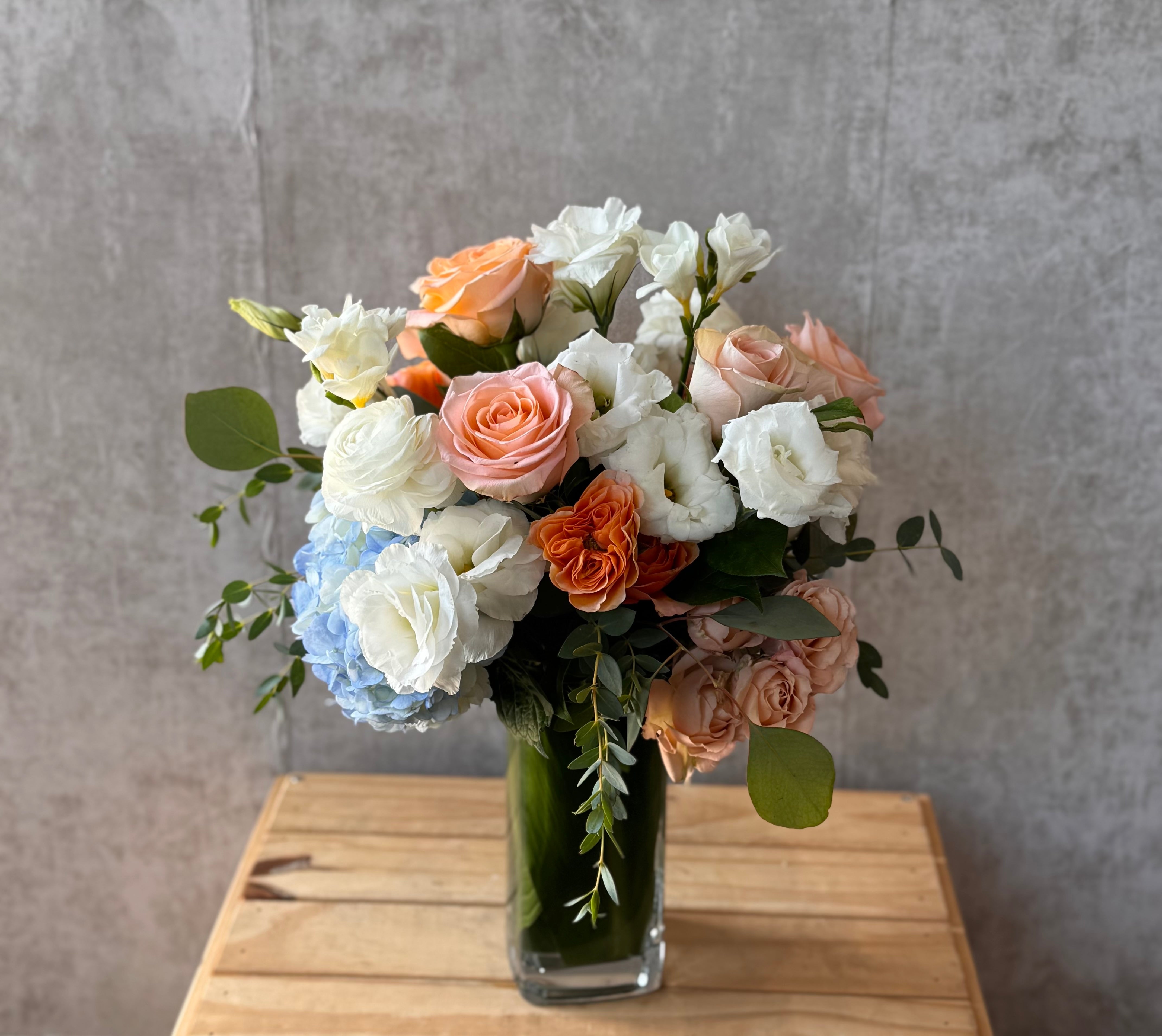 Bouquet of flowers in a clear vase on a wooden surface with a gray background