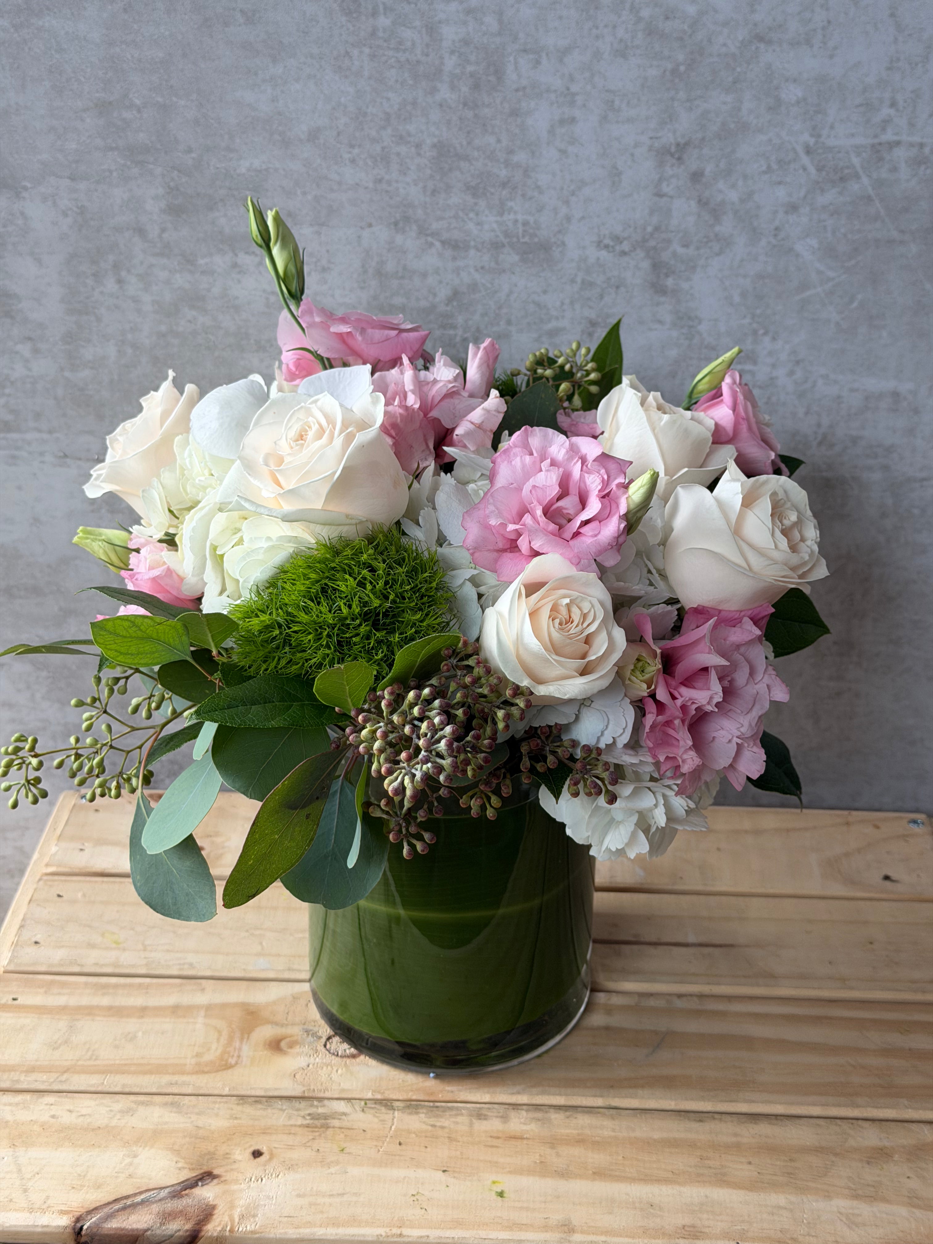 Bouquet of pink and white flowers in a green vase on a wooden surface with a gray background