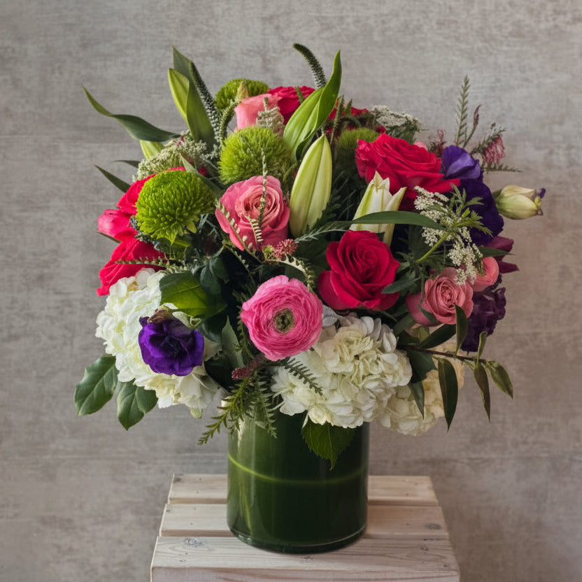Bouquet of colorful flowers in a green vase on a wooden surface with a gray background