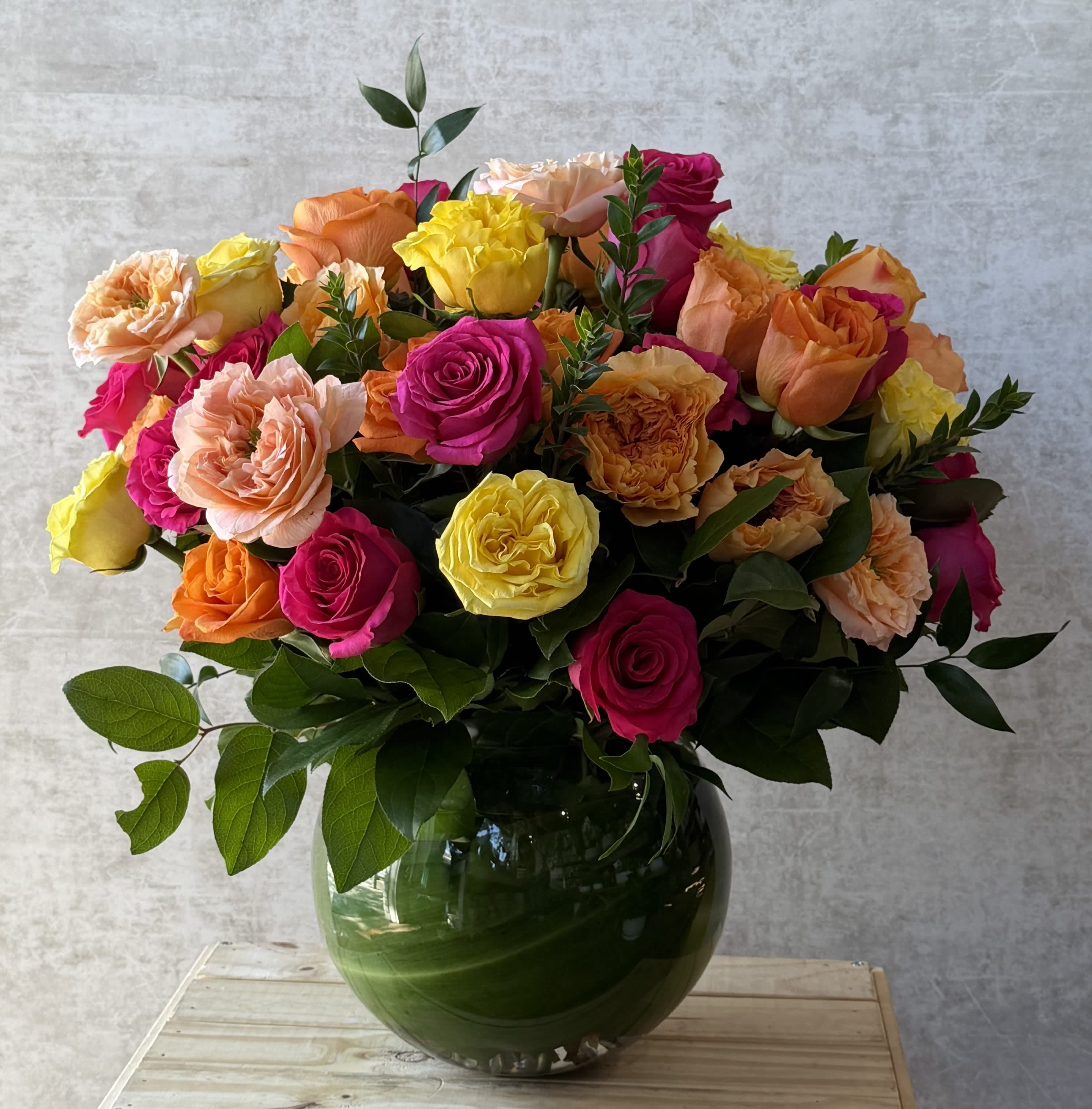 Bouquet of colorful flowers in a green vase on a wooden surface with a gray background